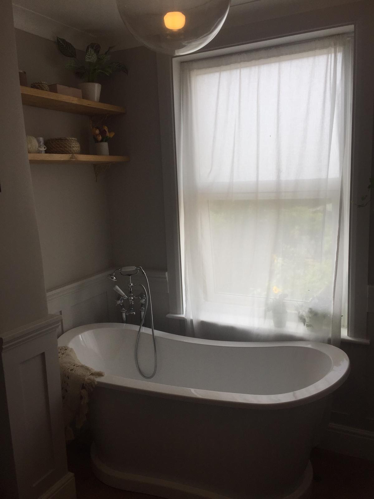 Art deco bath by a large sash window and two wooden shelves above the bath.