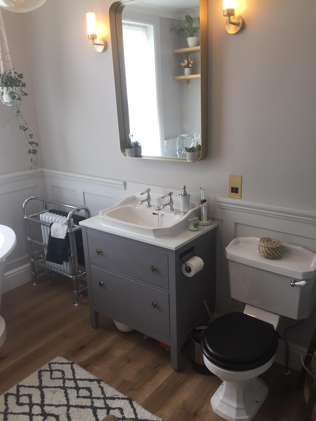 Grey art deco sink, toilet with black seat and towel rail. Large mirror above the sink with two lights.